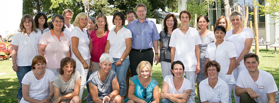 Eine Gruppe von Menschen steht und kniet auf einer Rasenfläche im Freien und lächelt für ein Gruppenfoto.