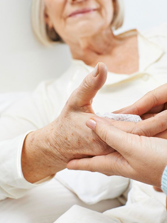 Die Hände einer Person halten sanft die Hand einer anderen Person und tragen Creme darauf auf.