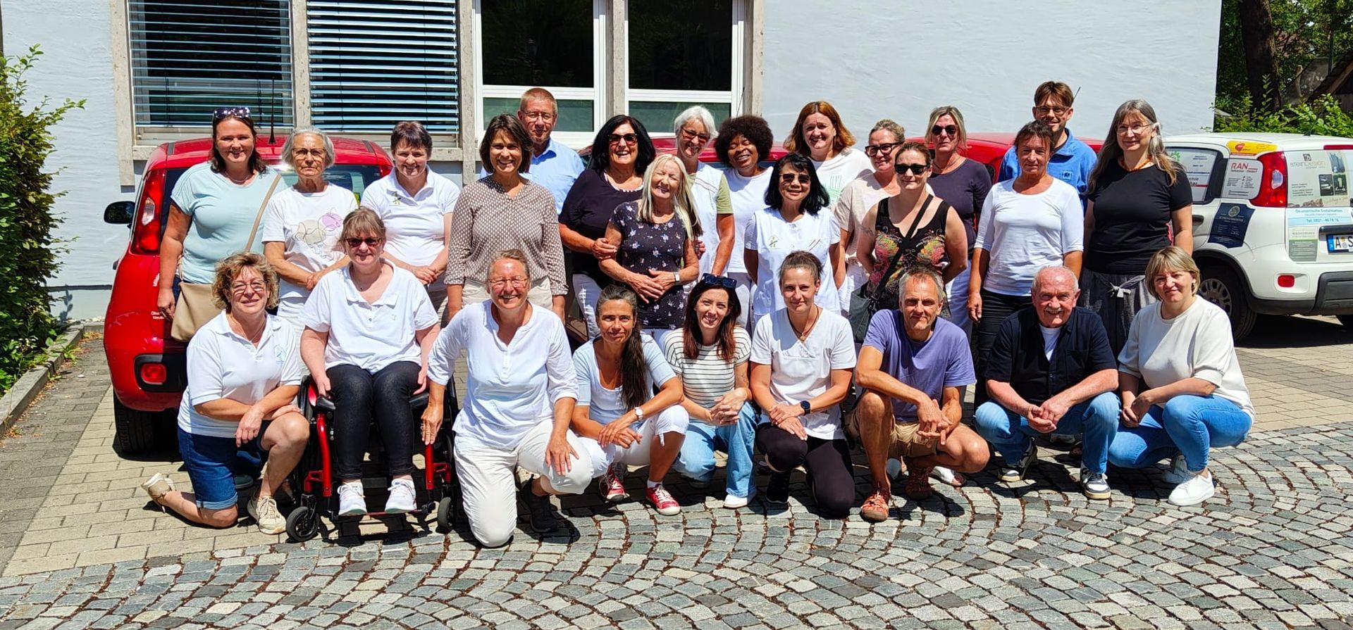 Eine Gruppe von Menschen steht und kniet auf einer Rasenfläche im Freien und lächelt für ein Gruppenfoto.
