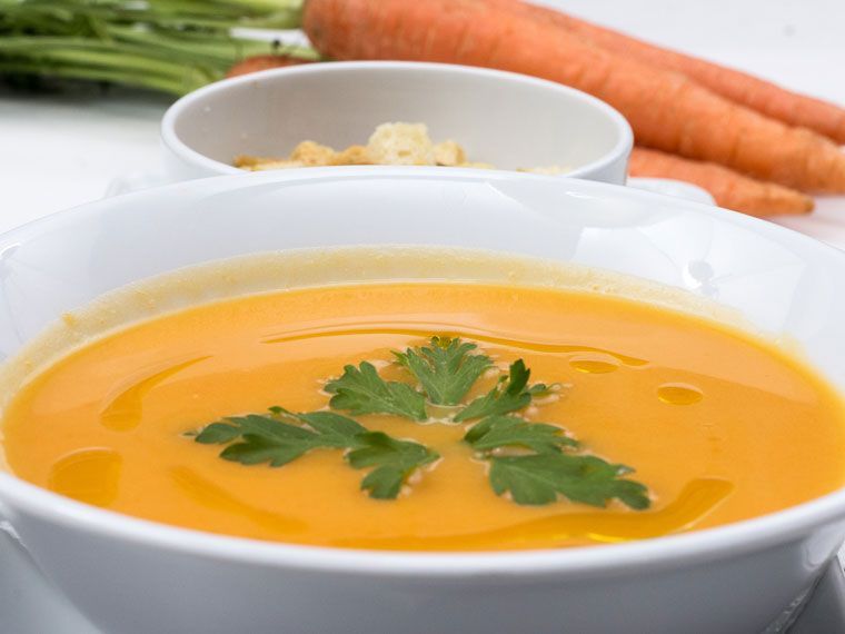 Eine weiße Schüssel mit cremiger Orangen-Karotten-Suppe, garniert mit einem Petersilienzweig