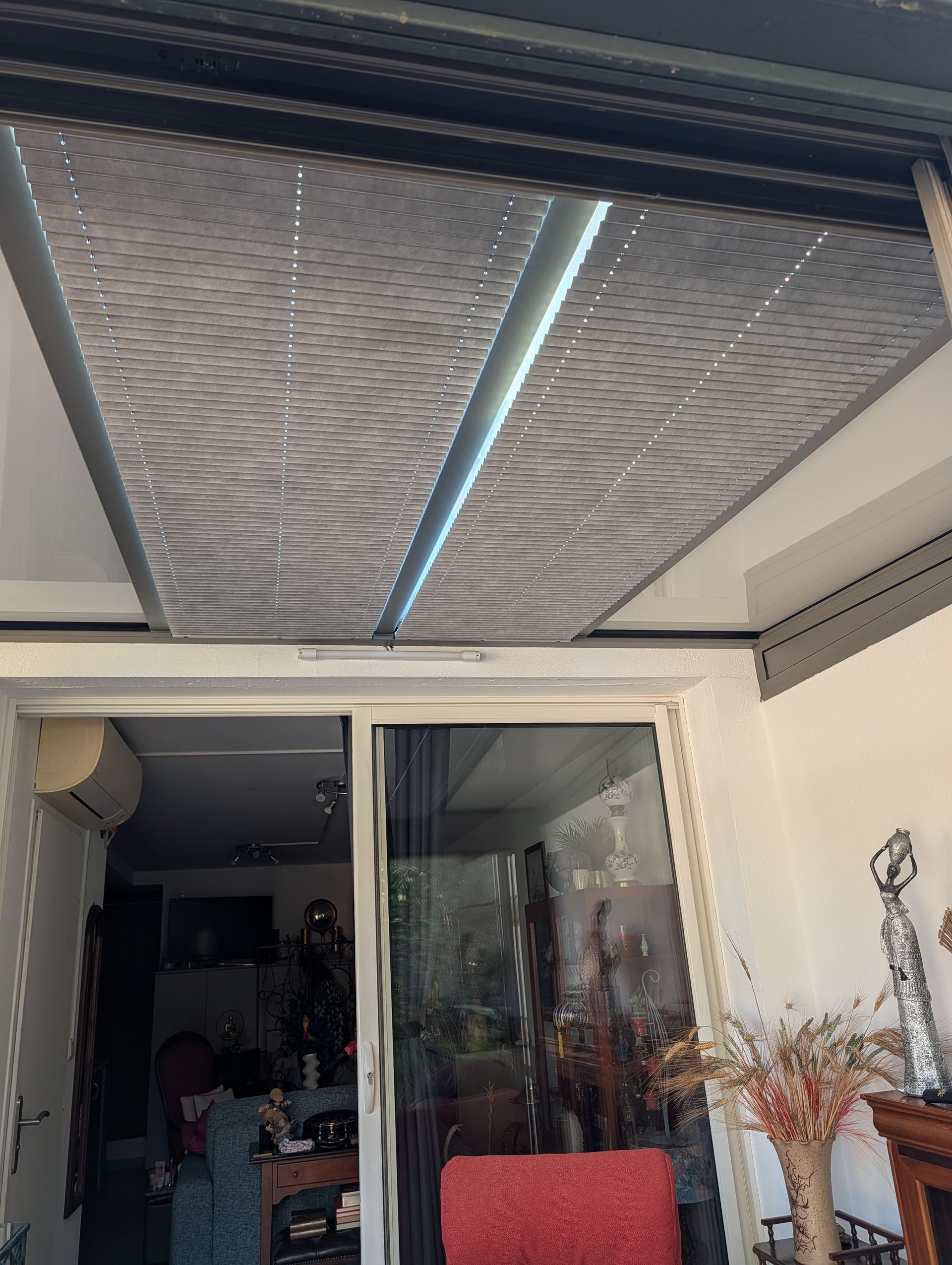 Vue depuis une terrasse donnant sur un salon avec un auvent gris texturé au plafond, à travers des portes coulissantes en verre.