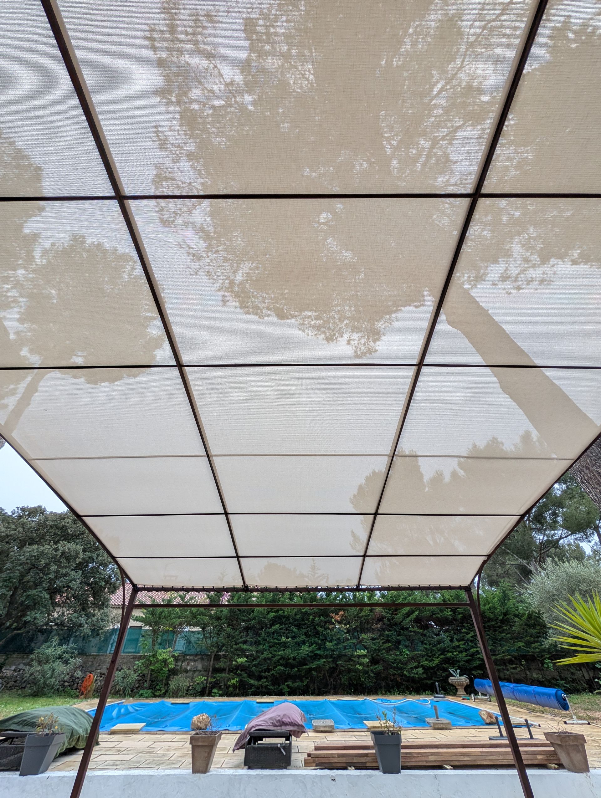 Une toile d'ombrage rectangulaire beige recouvre une piscine dans le jardin.