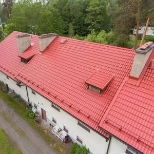 Ilmakuva pitkästä, punaisella metallikatolla varustetusta rakennuksesta metsän vieressä
