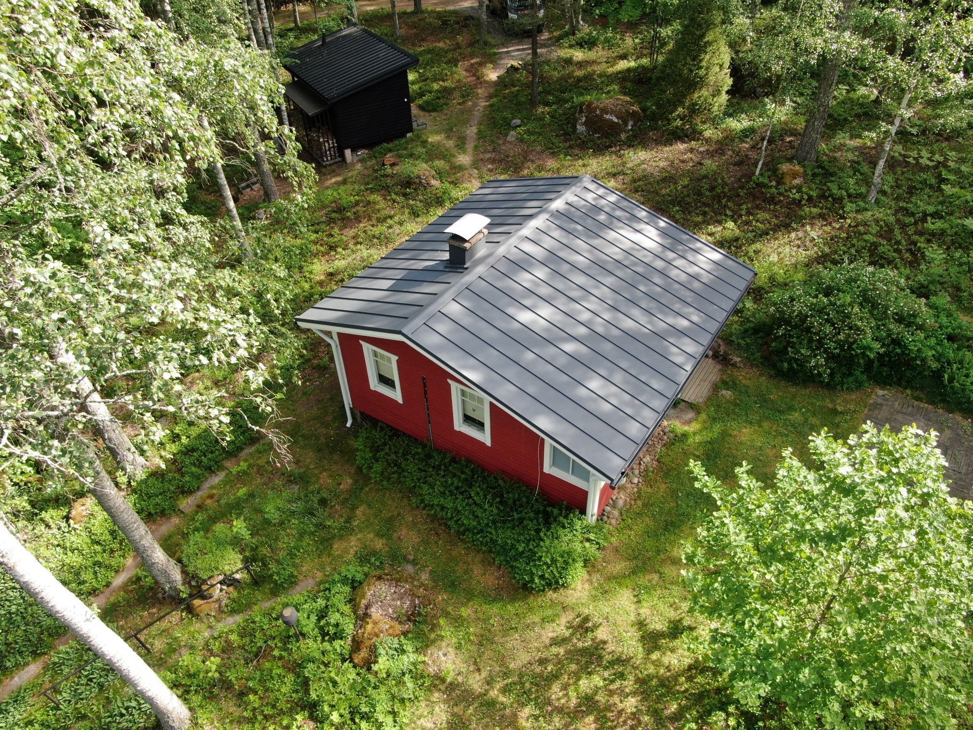 Ilmakuva punaisesta mökistä, jossa on harmaa katto, metsäisellä alueella.