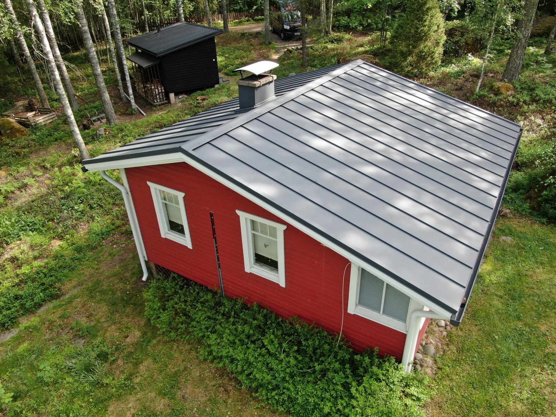 Pieni punainen vaja, jossa on harmaa metallikatto, ylhäältä katsottuna metsäisellä pihalla.