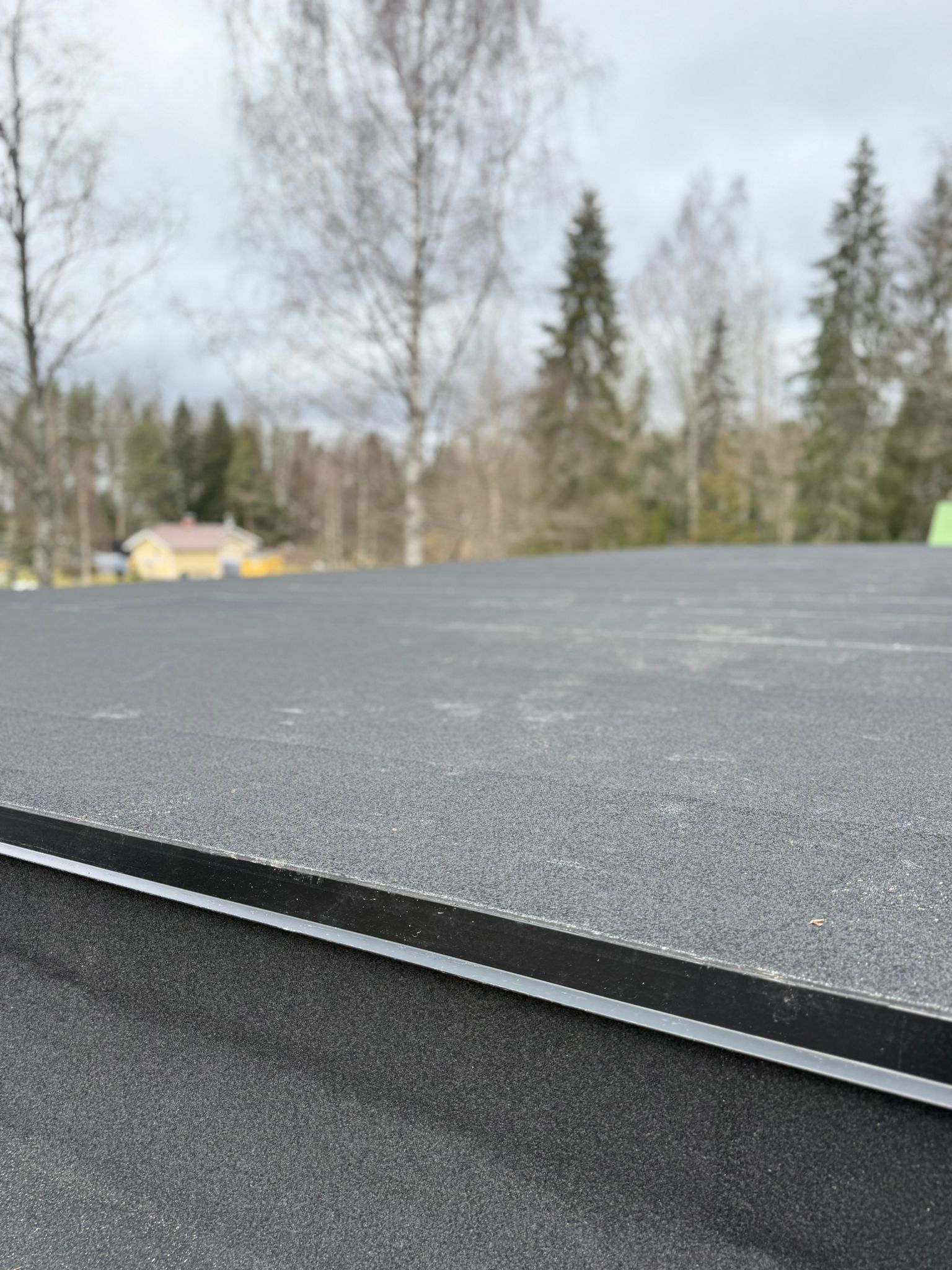 Lähikuva mustasta paanukatoista, jonka taustalla on puita ja pilvinen taivas