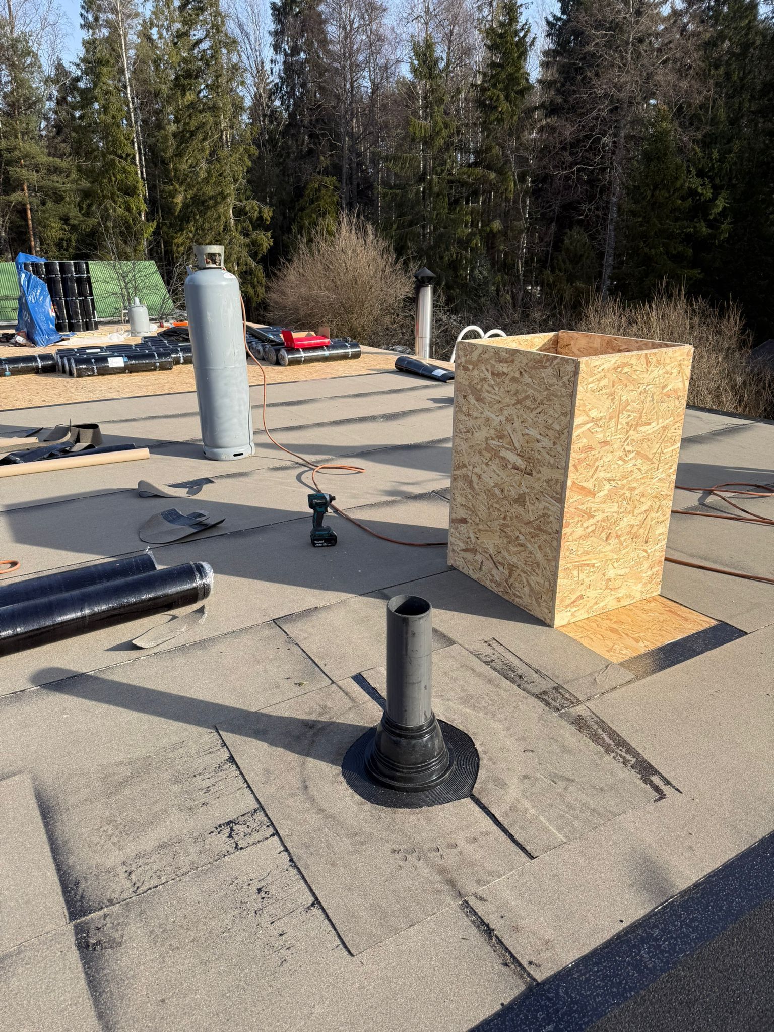 Katolla tuuletusaukkoja ja vanerilaatikko, työkaluja ja materiaaleja hajallaan metsäalueen lähellä.