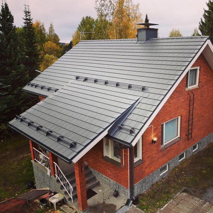 Punainen talo, jossa on jyrkkä harmaa metallikatto ja kattoikkunat puiden keskellä