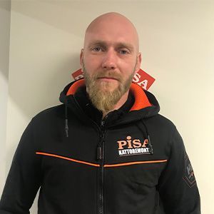 Mustaoranssiin PISA-takkiin pukeutunut mies seisoo yksinkertaista seinää vasten