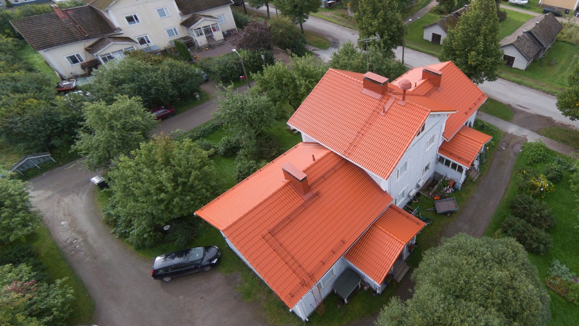 Ilmakuva valkoisesta, punakattoisesta talosta puiden ja naapurirakennusten ympäröimänä.