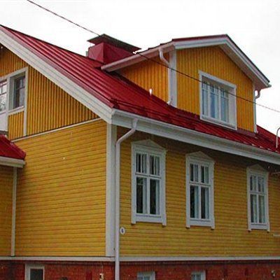 Keltainen talo punaisella katolla ja valkoreunaisilla ikkunoilla pilvistä taivasta vasten