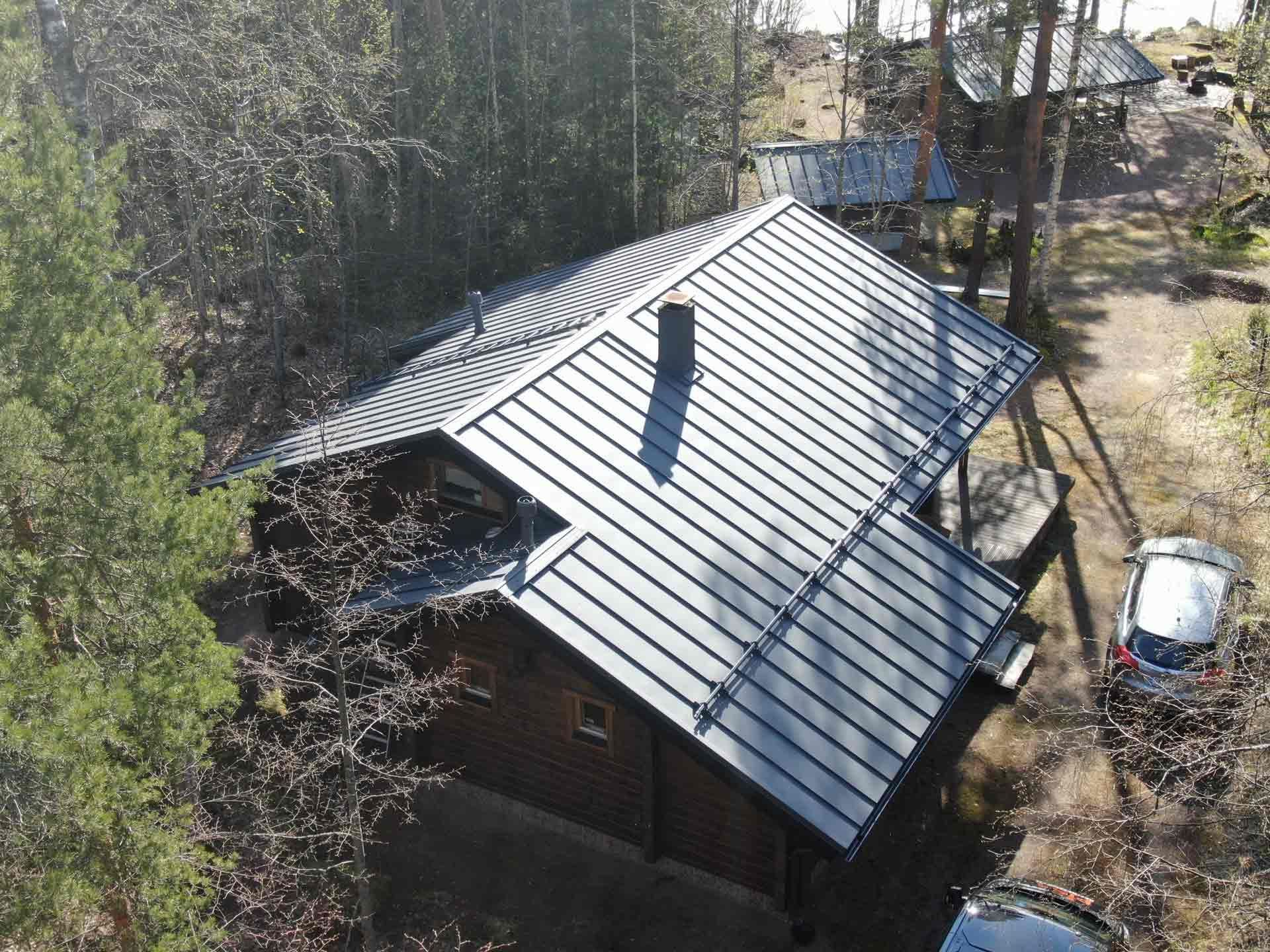 Ilmakuva talosta, jossa on harmaa metallikatto ja jota ympäröivät puut ja piha.