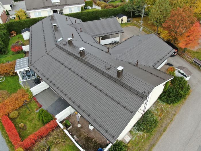 Ilmakuva modernista harmaakattoisesta talosta, jota ympäröivät puut ja asuinkatu.