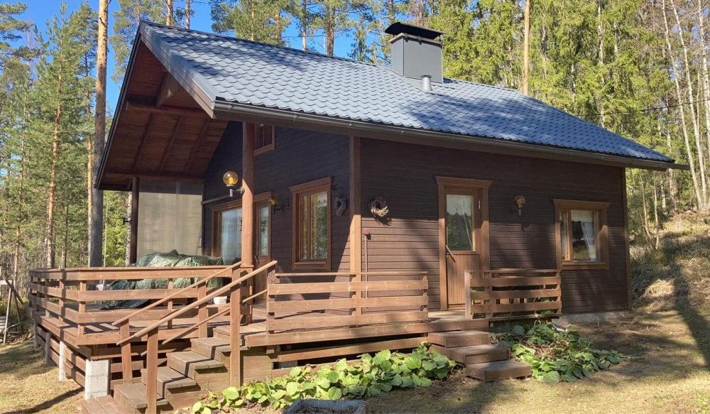 Puinen mökki, jossa on kuisti ja portaat aurinkoisessa metsäympäristössä