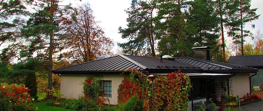 Yksikerroksinen talo tummalla katolla, syksyisten puiden ja punavihreiden köynnösten ympäröimänä.