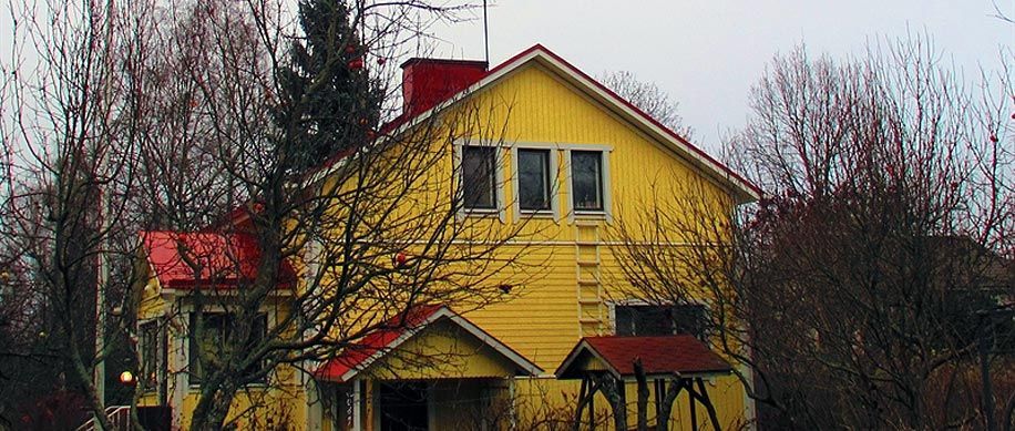 Keltainen talo punaisella katolla ja paljailla puilla pilvisellä pihalla