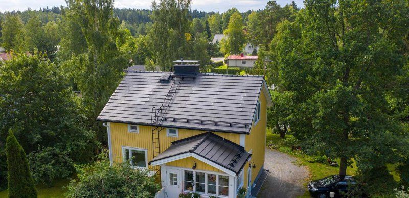 Keltainen talo harmaalla katolla, tiheiden vihreiden puiden ympäröimänä ylhäältä katsottuna
