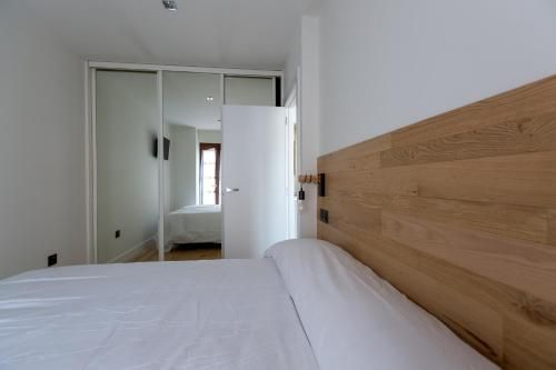 Dormitorio con cama, cabecero de madera clara, ropa de cama blanca y armario con puertas espejadas.