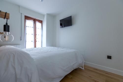 Dormitorio con ropa de cama blanca, suelo de madera y televisor de pared.
