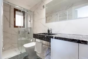 Baño moderno con paredes de mármol, ducha de cristal, encimera negra, lavabo blanco y ventana.