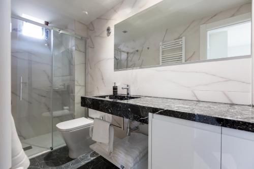 Baño moderno con paredes de mármol, ducha de cristal, encimera negra y espejo grande.