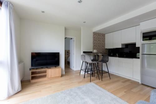 Espacio luminoso con cocina abierta, suelos de madera clara y televisor sobre un soporte de madera.