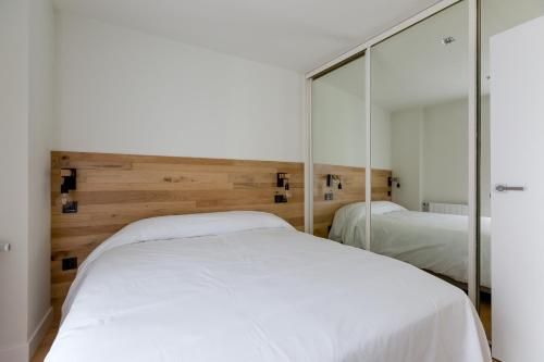 Dormitorio con ropa de cama blanca, cabecero de madera y puertas de armario con espejo.