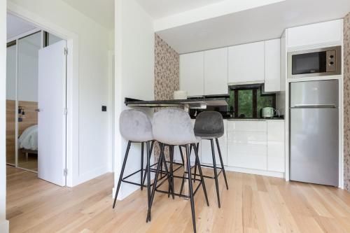 Cocina moderna con armarios blancos, barra americana con taburetes y frigorífico de acero inoxidable.