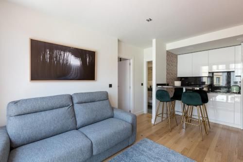 Sala de estar con sofá gris, cocina con taburetes de bar y obras de arte en la pared.