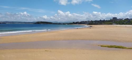 Playa de arena dorada, agua azul y algunas personas bajo un cielo azul nublado. Al fondo se divisa una ciudad.