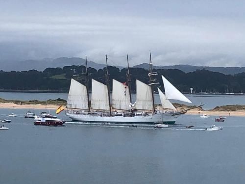 Velero blanco de gran altura con cuatro mástiles en el agua, con barcos de apoyo.