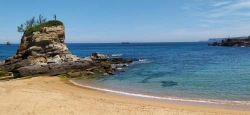 Escena de playa con una isla rocosa, agua azul y cielo despejado.