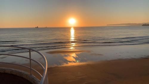 Atardecer sobre el océano, olas que rompen en la playa, luz del sol reflejándose en el agua y la arena.