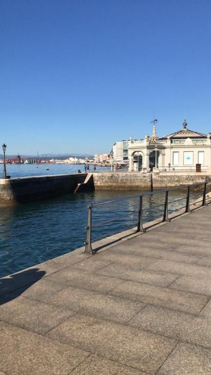 Vista del puerto con paseo marítimo de piedra, agua y ornamentado edificio blanco bajo un cielo azul despejado.