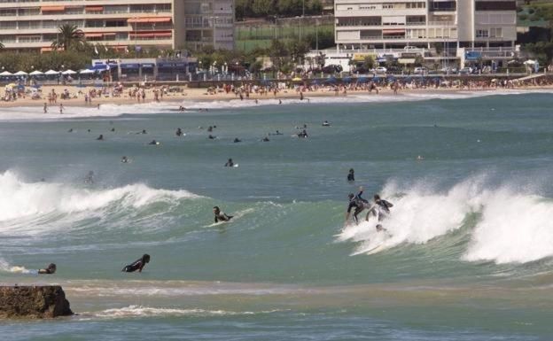 Surfistas cabalgando olas en el océano cerca de una playa abarrotada con edificios al fondo.