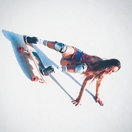 Mujer practicando skateboarding, realizando un body slide. Lleva rodilleras y calcetines, con los brazos extendidos.