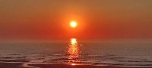 Atardecer sobre el océano, con el reflejo del sol centelleando sobre el agua. Tonos naranjas y dorados dominan el cielo.