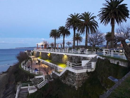 Paseo marítimo con palmeras, una balaustrada blanca y vistas al océano al atardecer.