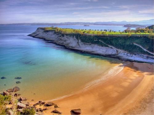 Playa de arena dorada y agua turquesa, bajo un acantilado blanco con hierba verde, bajo un cielo azul.