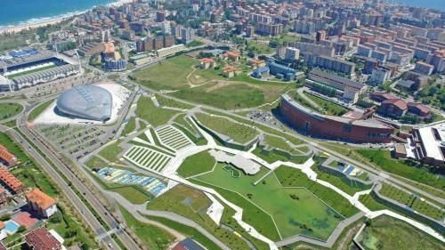 Vista aérea de una ciudad costera con arquitectura moderna, espacios verdes y un estadio.