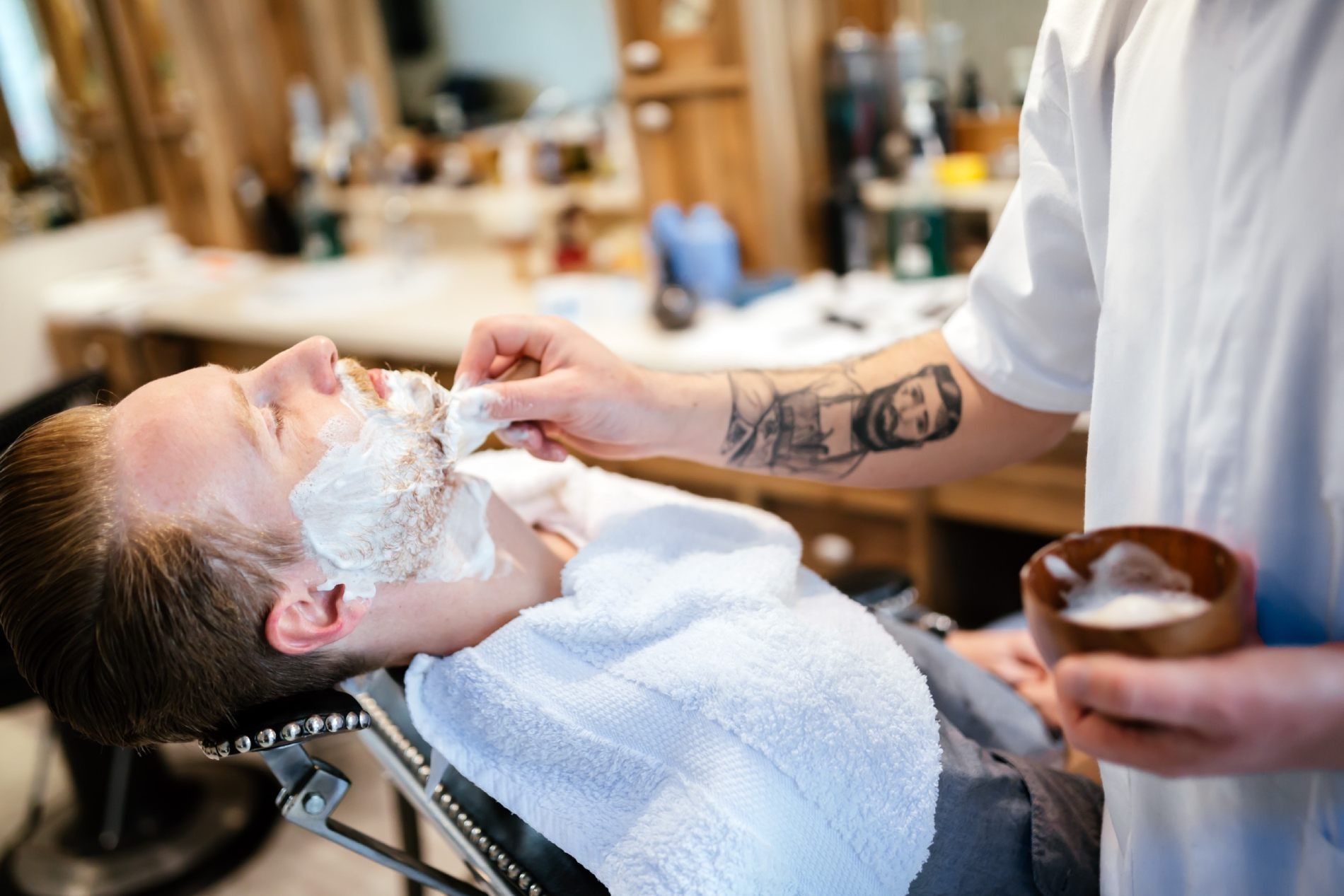 Barbero aplicando crema de afeitar en la cara de un hombre en una barbería.