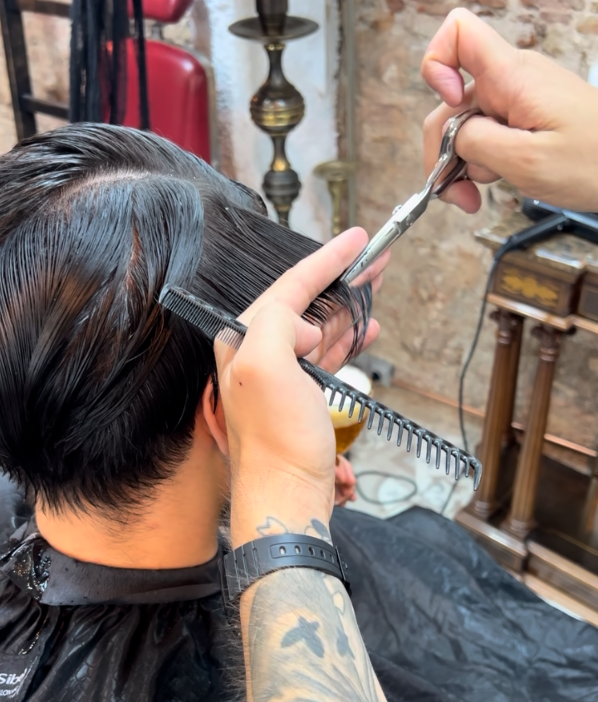 Barbero cortando pelo oscuro con tijeras y peine. Primer plano, en interiores.