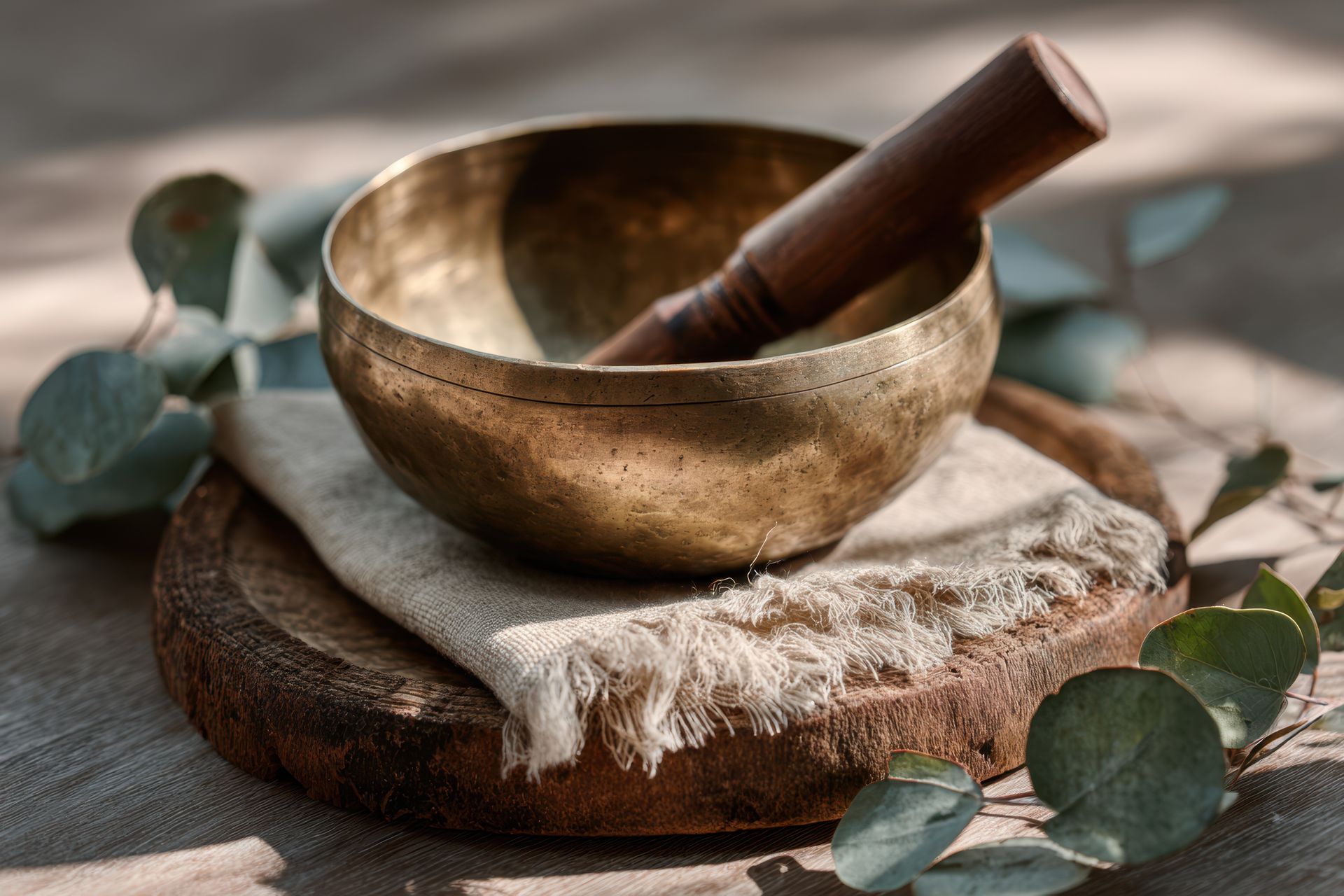 Bol chantant doré avec maillet, tissu de lin et eucalyptus sur un plateau en bois.