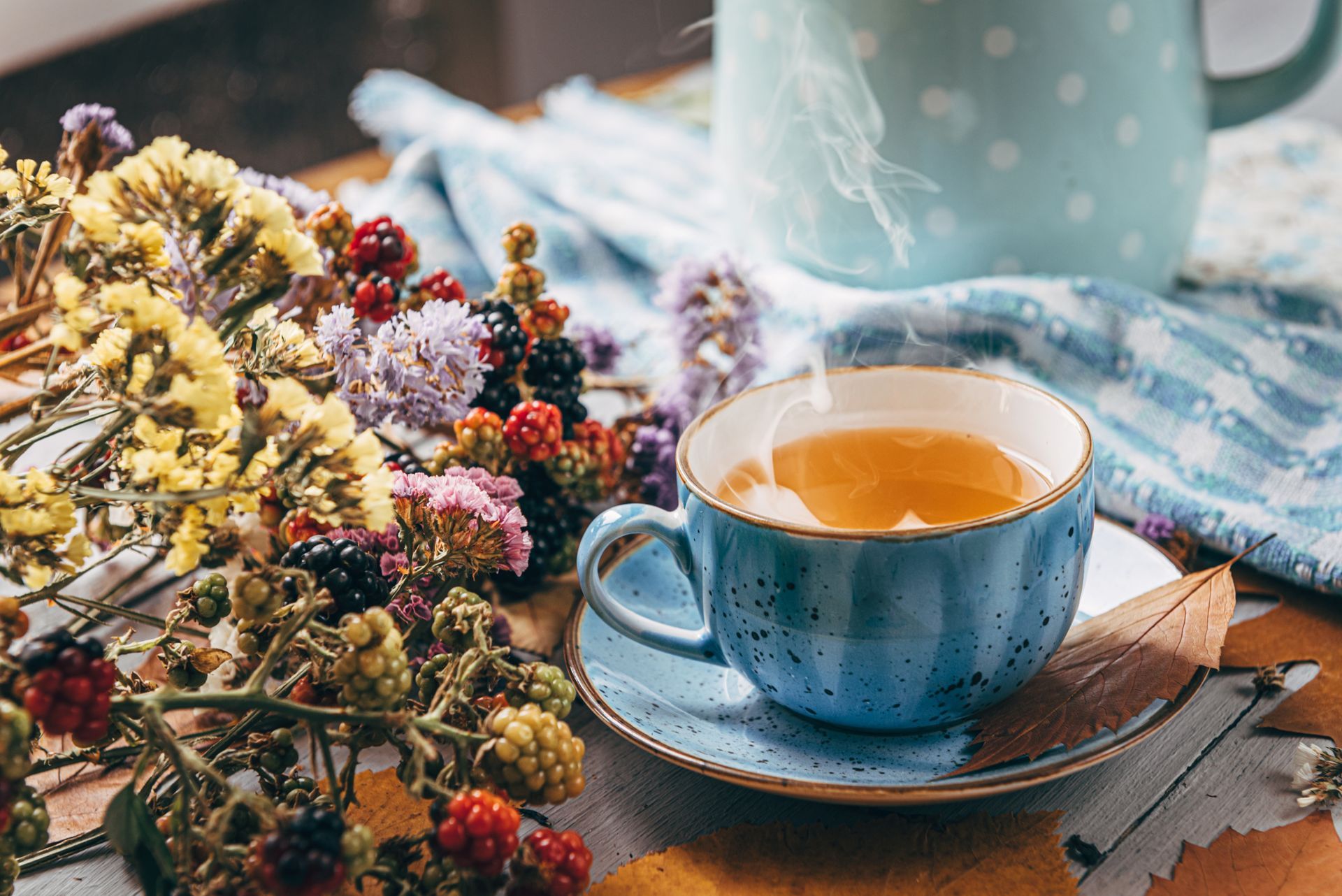 Tasse bleue avec thé, soucoupe, fleurs et mug. De la vapeur s'élève, suggérant la chaleur.
