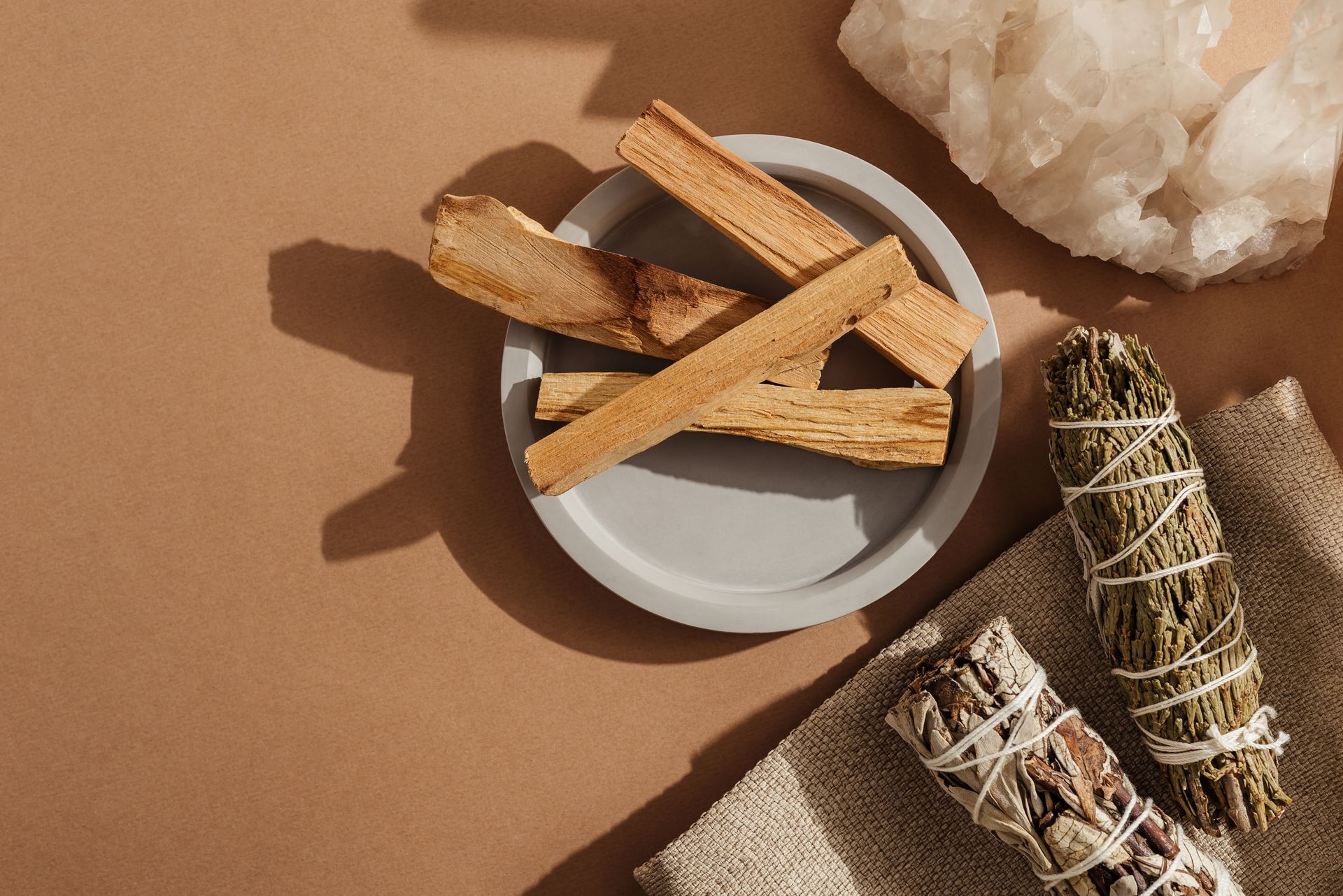 Disposition de bâtonnets de Palo Santo, de fagots de sauge et de cristaux sur une surface brune.