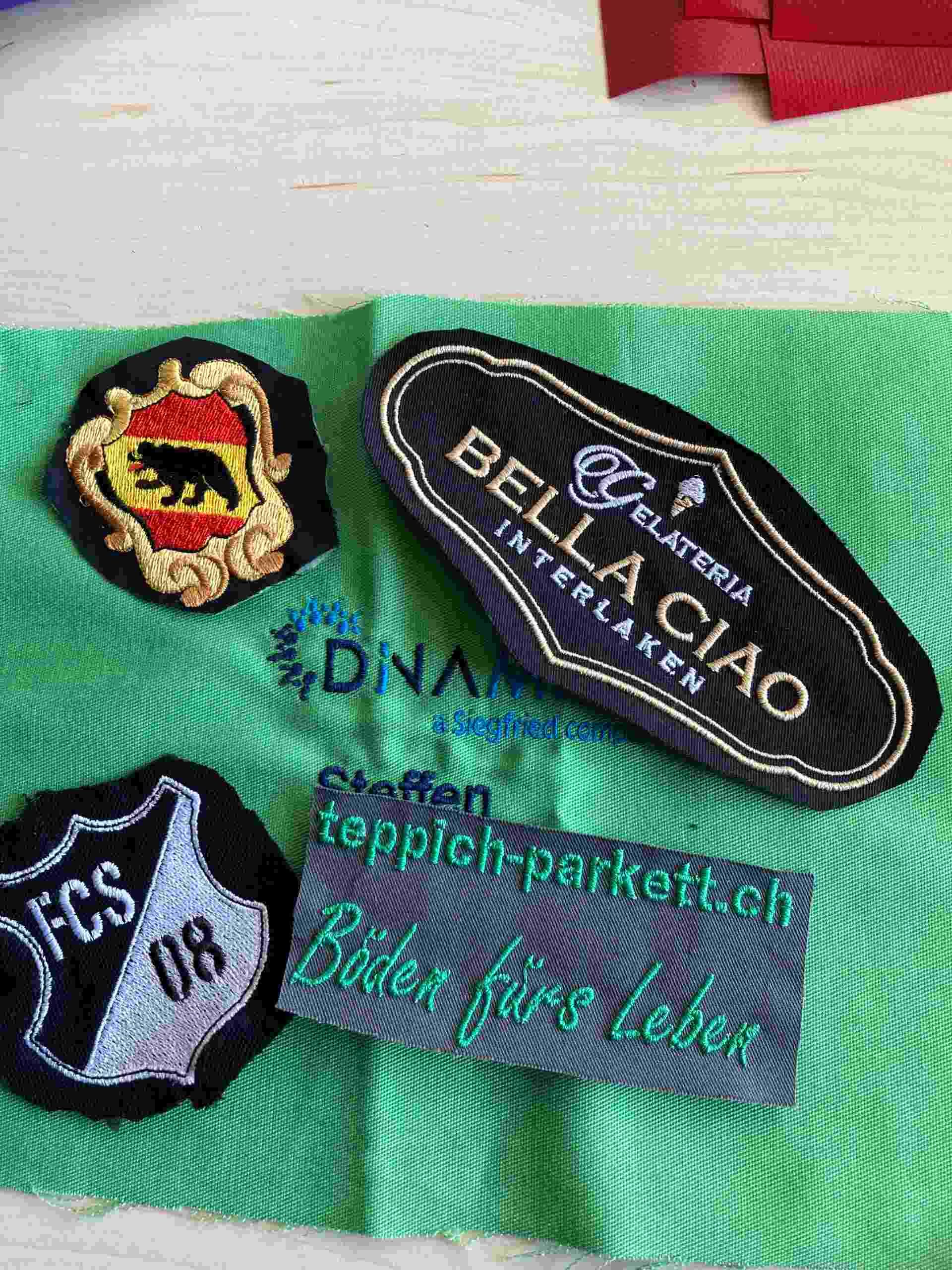 Aufnäher mit gestickten Texten und Logos in verschiedenen Formen und Farben auf grünem Stoff.