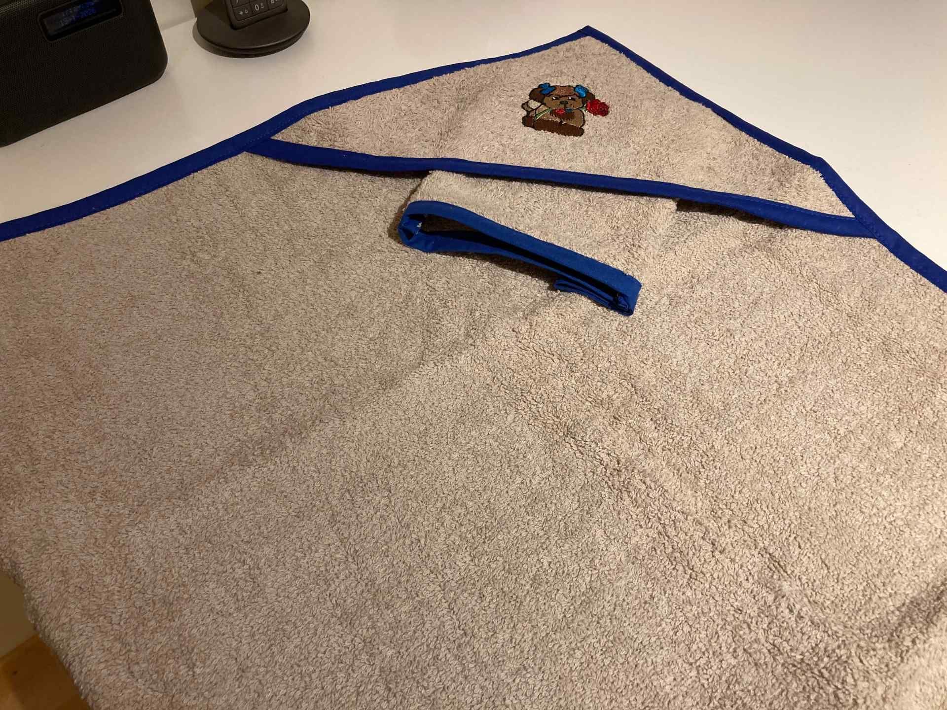 Beigefarbenes Kapuzenhandtuch mit blauem Saum und einem kleinen Hundemotiv.