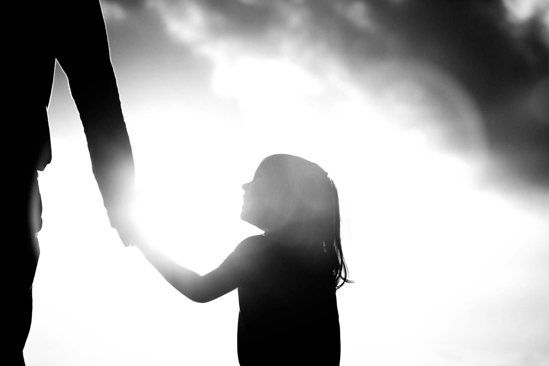 Petite fille à contrejour tenant la main de son parent