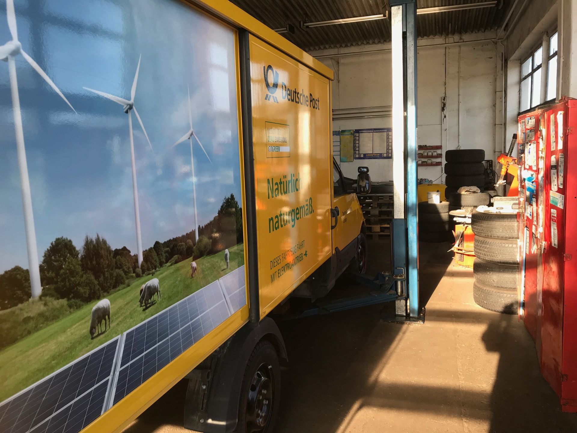 Ein gelber Lastwagen mit einem Bild von Windmühlen und Sonnenkollektoren an der Seite parkt in einer Garage.