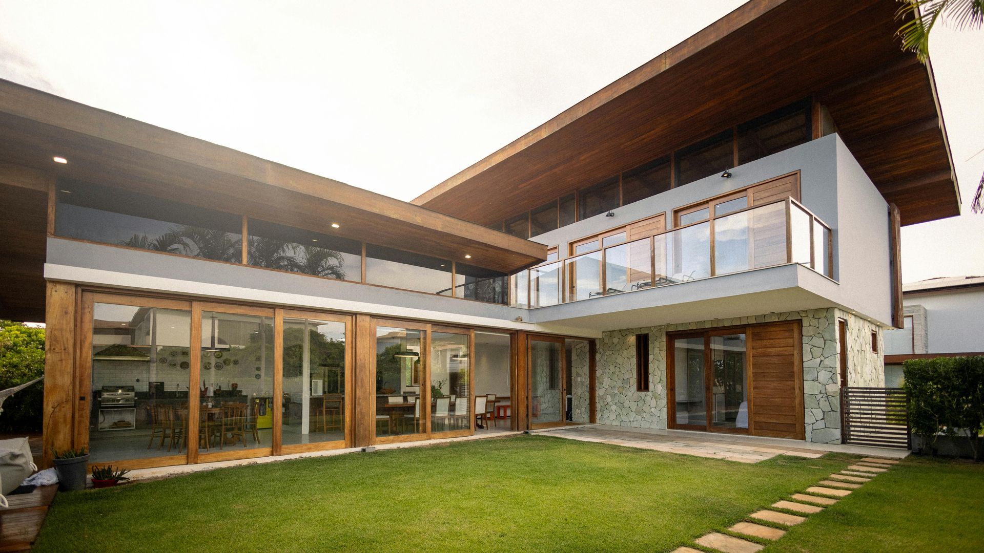 Una casa moderna de dos plantas con grandes ventanales y techo de madera con vistas a un frondoso césped verde.